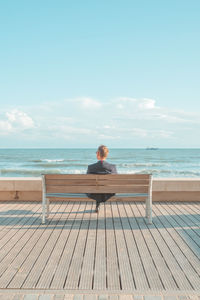 Man sitting on wooden pier looking at sea against sky