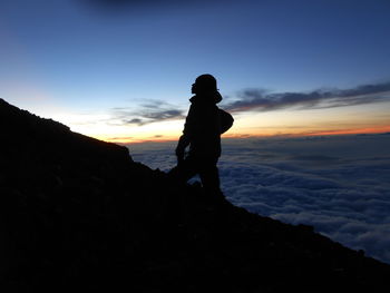 Silhouette man standing on rock against sky during sunset