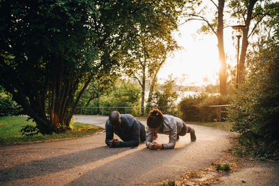 Male and female athletes doing planks on road in park during sunset