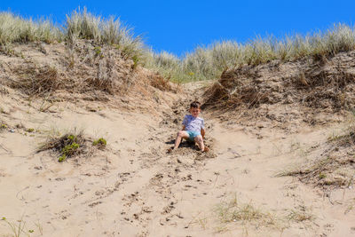 Full length of boy sliding on sandy slope 