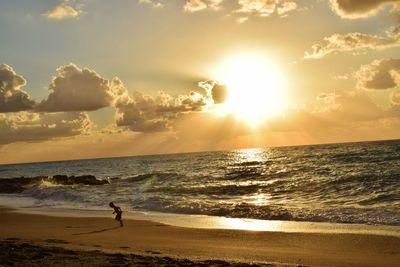 Silhouette man standing on beach against sky during sunset