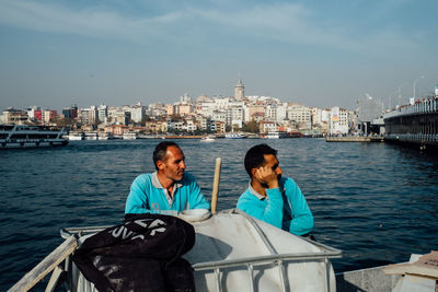 Woman sitting on boat in river with city in background