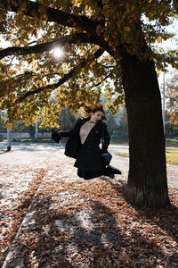 Woman standing by tree trunk during autumn