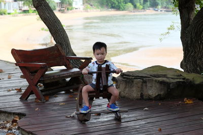 Cute boy sitting on rocking horse at wooden walkway