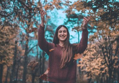 Portrait of smiling young woman standing in forest during autumn