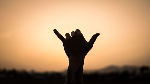Silhouette of woman's hand against sky during sunset