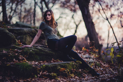 Full length of young woman sitting on rock in forest