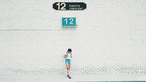 Full length of woman walking against wall with number and text