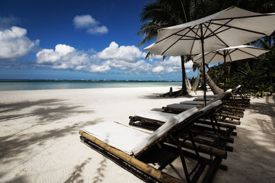 Lounge chairs by swimming pool at beach against sky