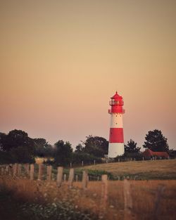 Lighthouse by sea against clear sky during sunset