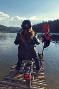 Rear view of woman with bicycle on pier over lake against sky