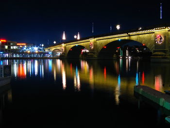 Illuminated bridge over river in city at night