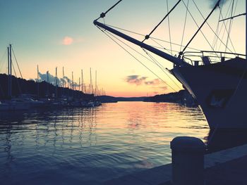 Sailboats moored in harbor at sunset