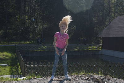Full length of girl tossing hair while standing against pond and trees