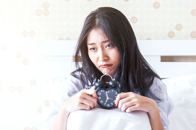 Young woman with alarm clock sitting on bed