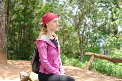 Woman looking away while sitting on tree