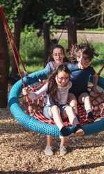 Portrait of a teenage girl pushing her sisters on a round rope swing in the park.