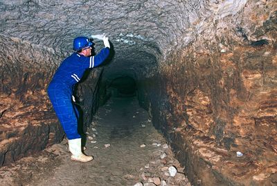 Worker in tunnel. staff in protective suit check sediments in rocky wall, large underground sewer