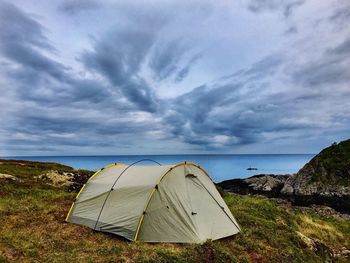 Tent in sea against cloudy sky