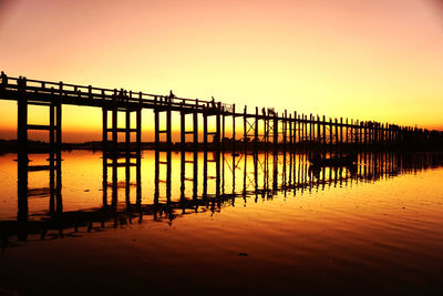 Silhouette pier on lake against orange sky