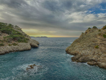 Cliff by sea against cloudy sky