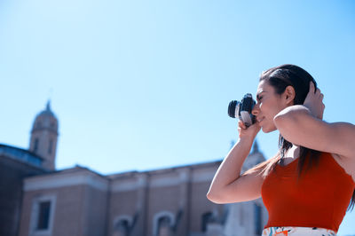 Low angle view of beautiful woman photographing by church against clear sky