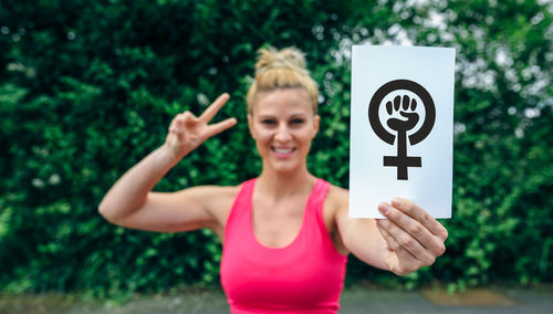 Portrait of smiling woman holding placard while standing against plants