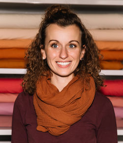 Portrait of a smiling woman standing in front of neatly arranged colorful fabric rolls 