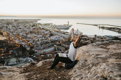 Man relaxing by sea in city against sky