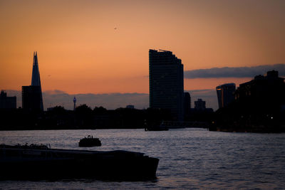 Silhouette buildings by sea against sky during sunset