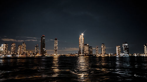 Illuminated buildings by sea against sky at night