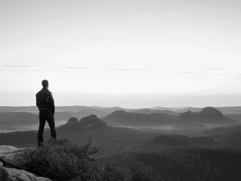 Rear view of man standing on mountain against sky