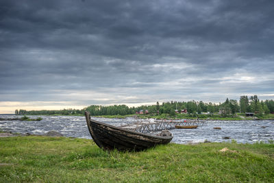 Abandoned boat on riverbank against cloudy sky