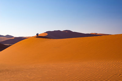 Rear view of woman crouching on desert against sky