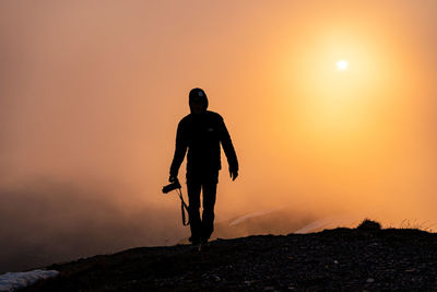 Silhouette man standing on ocean against sky during sunset