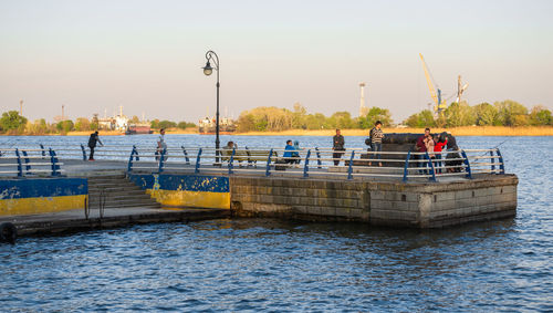 People on pier by river against sky