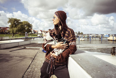 Strong asian woman stands at water dock with two small dogs in sun