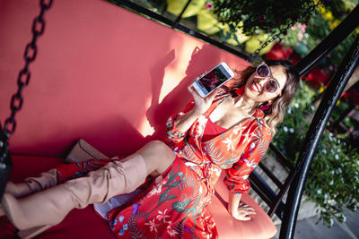 Portrait of young woman holding mobile phone while sitting on swing