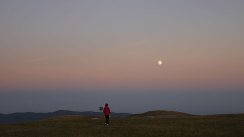 Woman standing on field against sky during sunset