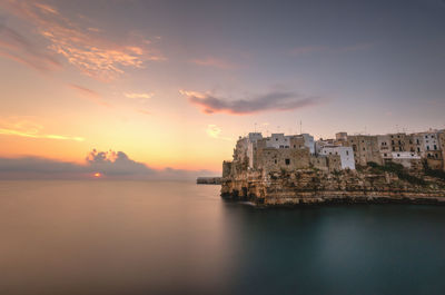 Buildings by sea against sky during sunset