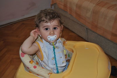 Portrait of cute baby boy sucking pacifier in walker at home