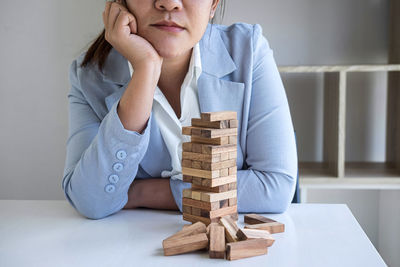 Midsection of businesswoman sitting by toy blocks on table against wall