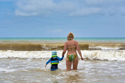 Full length of shirtless man in sea against sky