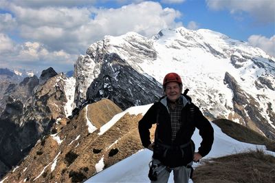 Portrait of senior man standing on snowcapped mountain against sky