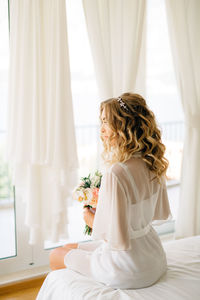 Young woman holding flower bouquet while sitting at home