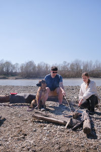 Friends sitting on beach against clear sky