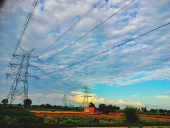 Electricity pylon on field against cloudy sky