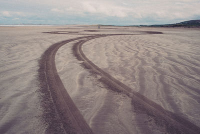 Tire tracks on sand dunes against sky