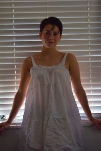 Portrait of a beautiful young woman standing against window