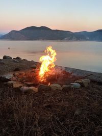 Bonfire by lake against clear sky at sunset
